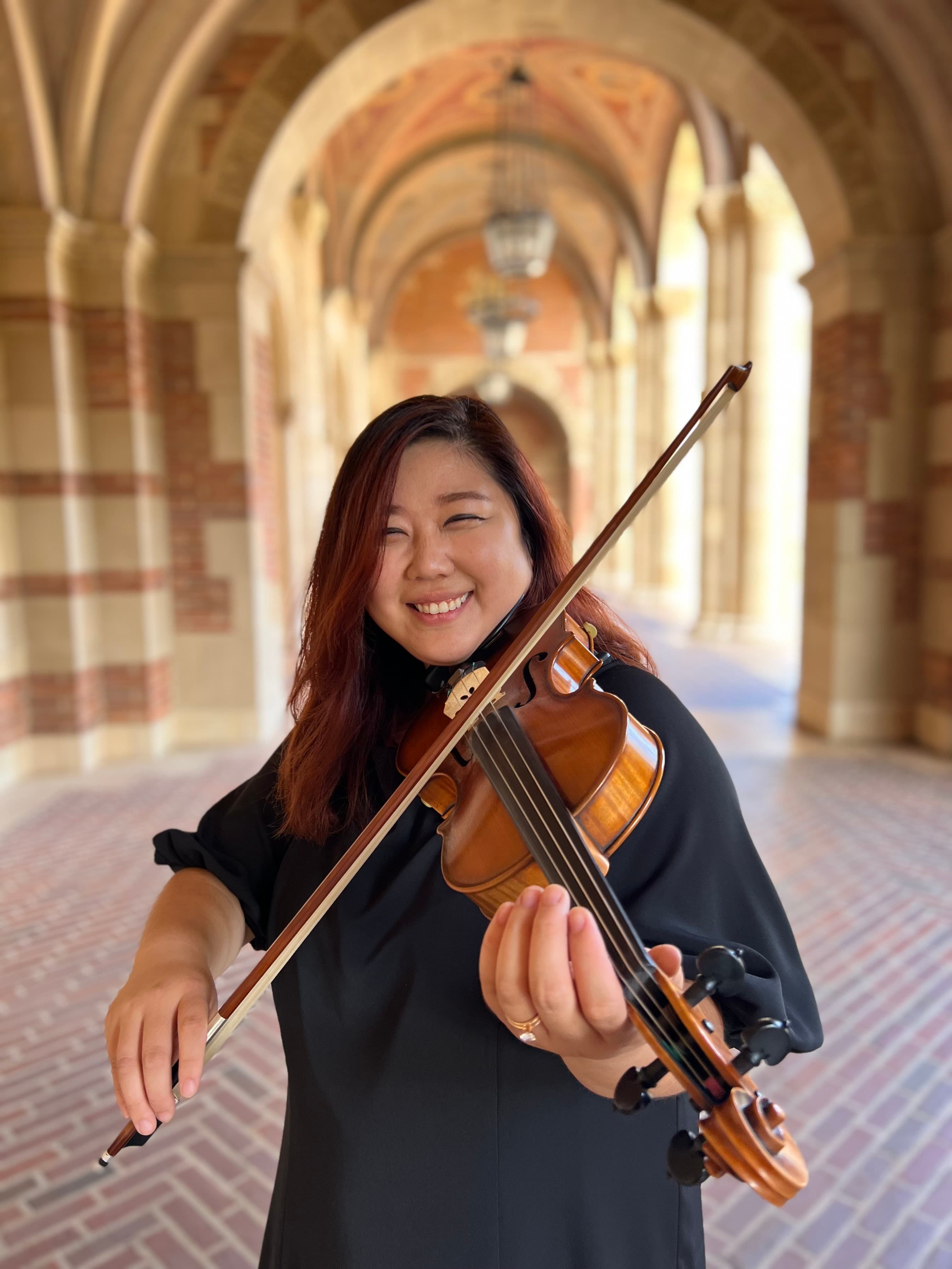 Fay You playing violin beneath a stone archway