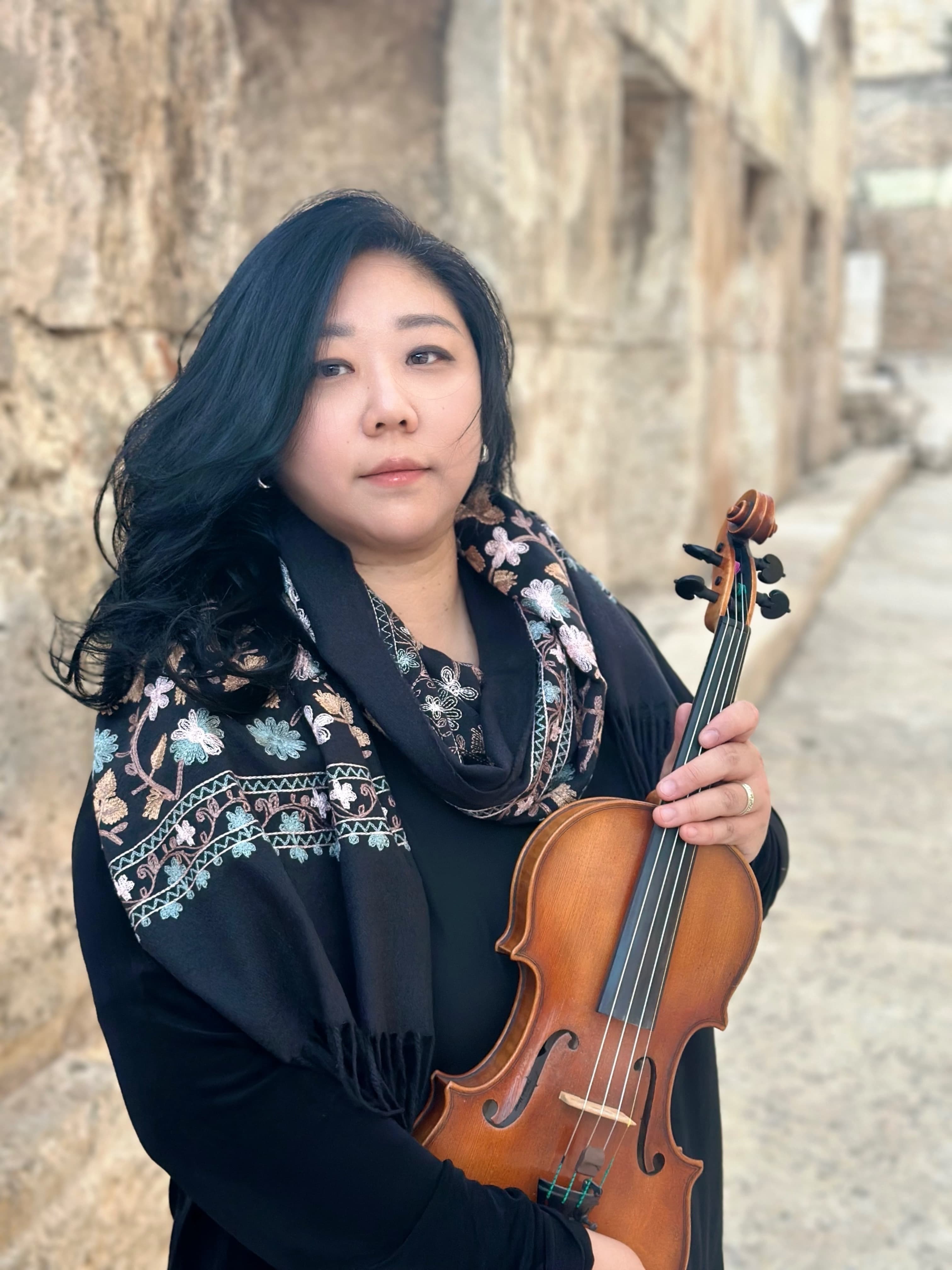 Fay You holding her violin against a stone wall